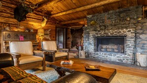 A rustic cabin interior with a stone fireplace, wooden furniture, and mounted animal heads. - Double L Bar Lodge Guest Ranch (Cody)