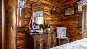 A wooden cabin interior with a dresser, a mirror, a potted plant, and a floral painting on the wall. - Double L Bar Lodge Guest Ranch (Cody)