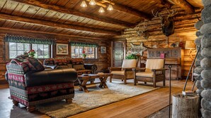 A log cabin interior with wooden floors, a leather sofa, a wooden chair, and a fireplace. - Double L Bar Lodge Guest Ranch (Cody)