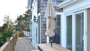 A wooden deck with a table and benches, a hanging umbrella, and a glass door leading to a covered area. - Luxurious Waterfront Retreat in Southampton: Breathtaking Views, Pool, and More! (Southampton)