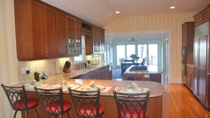 A spacious kitchen with wooden cabinets, a large island with bar stools, and a view to the dining area. - Luxurious Waterfront Retreat in Southampton: Breathtaking Views, Pool, and More! (Southampton)