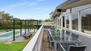 Eine moderne Außenterrasse mit Glastisch und -stühlen, mit Blick auf einen Swimmingpool und üppiges Grün.