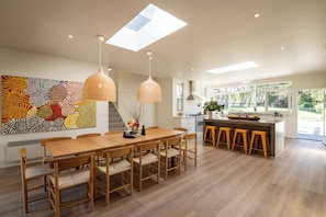 Una cocina moderna con tragaluz, un comedor con mesa y sillas de madera, y una barra con taburetes.