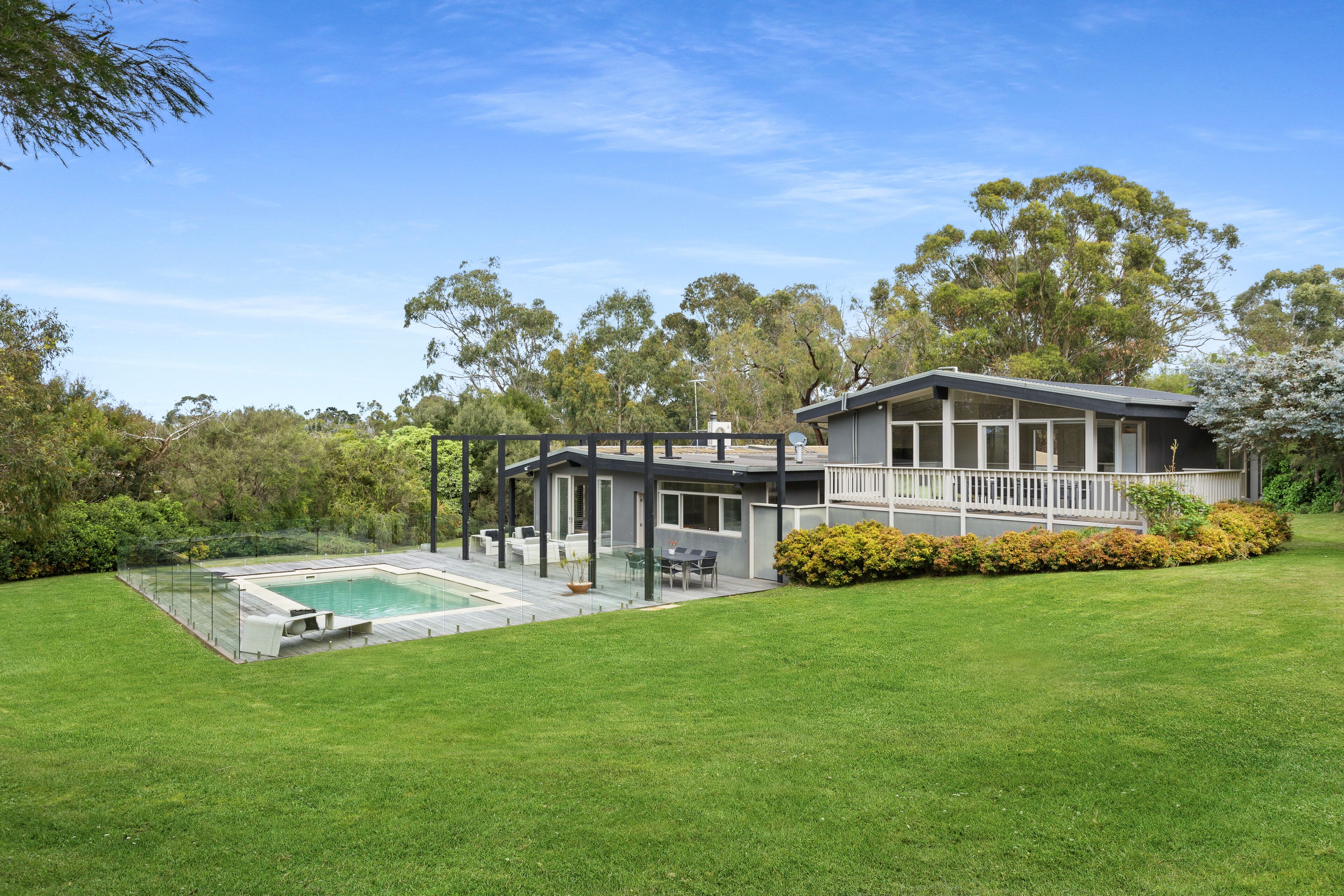 A modern house with a swimming pool, a covered patio, and a well-maintained lawn.
