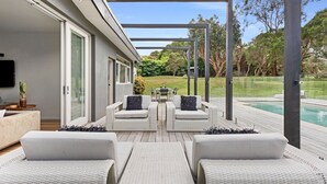 Eine moderne Terrassenanlage im Freien mit weißen Korbmöbeln, einem Pool und Blick auf die umliegende Bepflanzung.