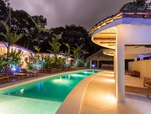 A swimming pool with lounge chairs and tropical plants, surrounded by a modern building with a curved roof. - 2 Bd Villa Mono Titi #3 at Rio Mono, Valle Pura Vida, Manuel Antonio (Quepos)