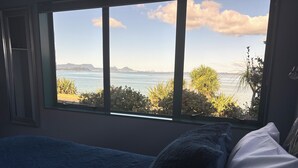 Een slaapkamer met een groot raam, een bed en uitzicht op een strand en bergen.