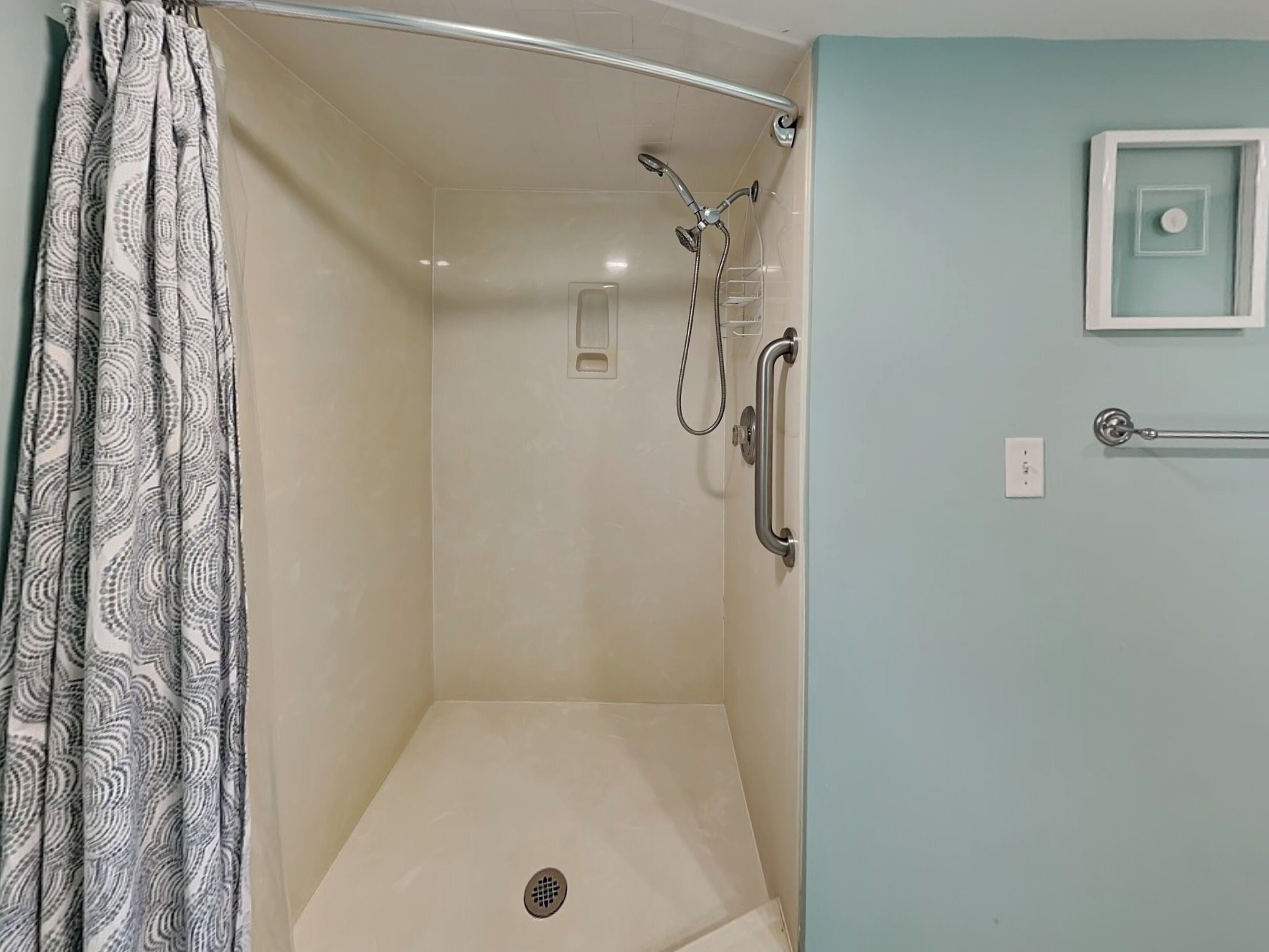 A shower with a glass door, a handrail, and a towel rack.