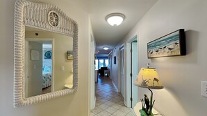 A hallway with a woven mirror, a lamp with a bird design, and a painting of birds on the wall. - Beachfront condo w. hot tub + beach access. (Tybee Island)