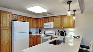 A kitchen with wooden cabinets, a white refrigerator, a microwave, a stove, and a sink. - Beachfront condo w. hot tub + beach access. (Tybee Island)