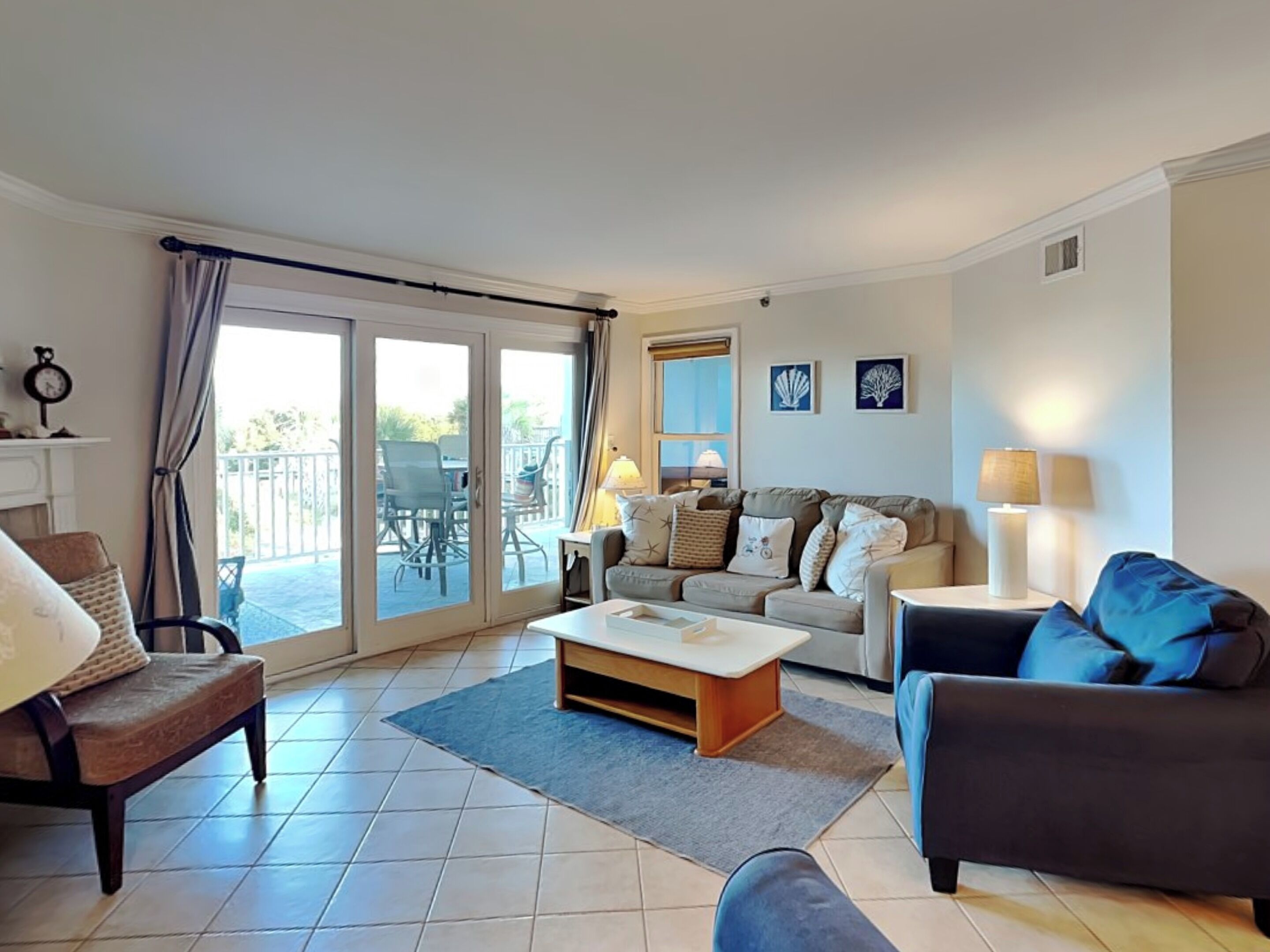 A living room with a sofa, armchair, and a coffee table. There is a balcony with outdoor furniture.