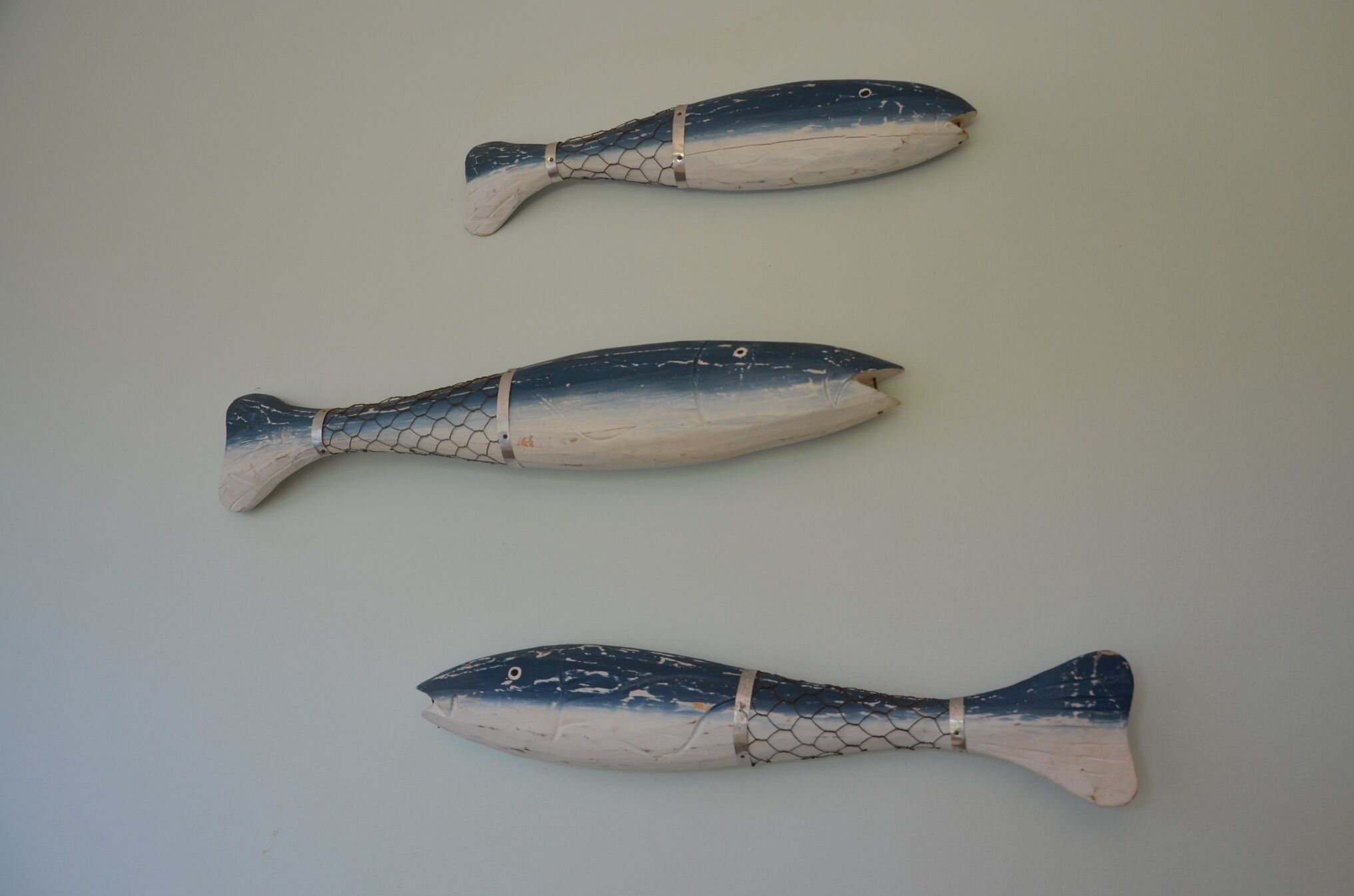 Three fish-shaped sculptures on a plain wall.