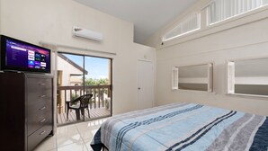 A bedroom with a bed, a TV on a dresser, a balcony, and a door leading outside.