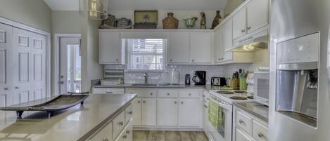 Una cocina con armarios blancos, un refrigerador de acero inoxidable y una lámpara colgante.