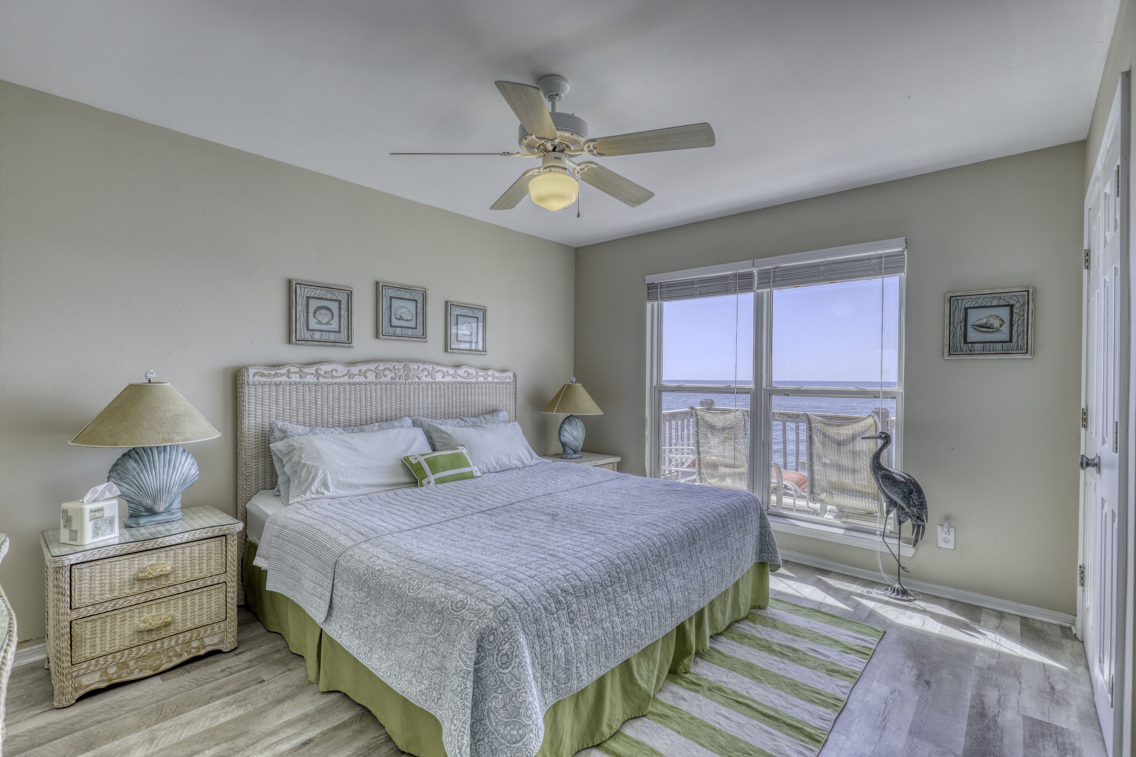 A bedroom with a large bed, a ceiling fan, a window with a view, and a decorative bird statue.