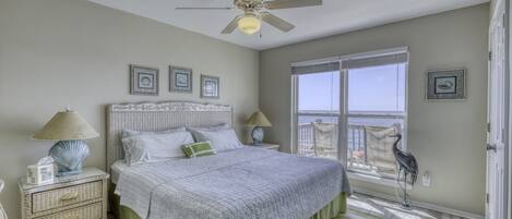 A bedroom with a large bed, a ceiling fan, a window with a view, and a decorative bird statue.