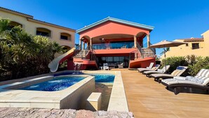 Ein Resort mit Poolbereich, Liegestühlen und einem zweistöckigen Gebäude mit roter Fassade.