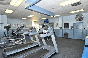 Academia com esteiras, bicicletas ergométricas e uma tela de televisão.
