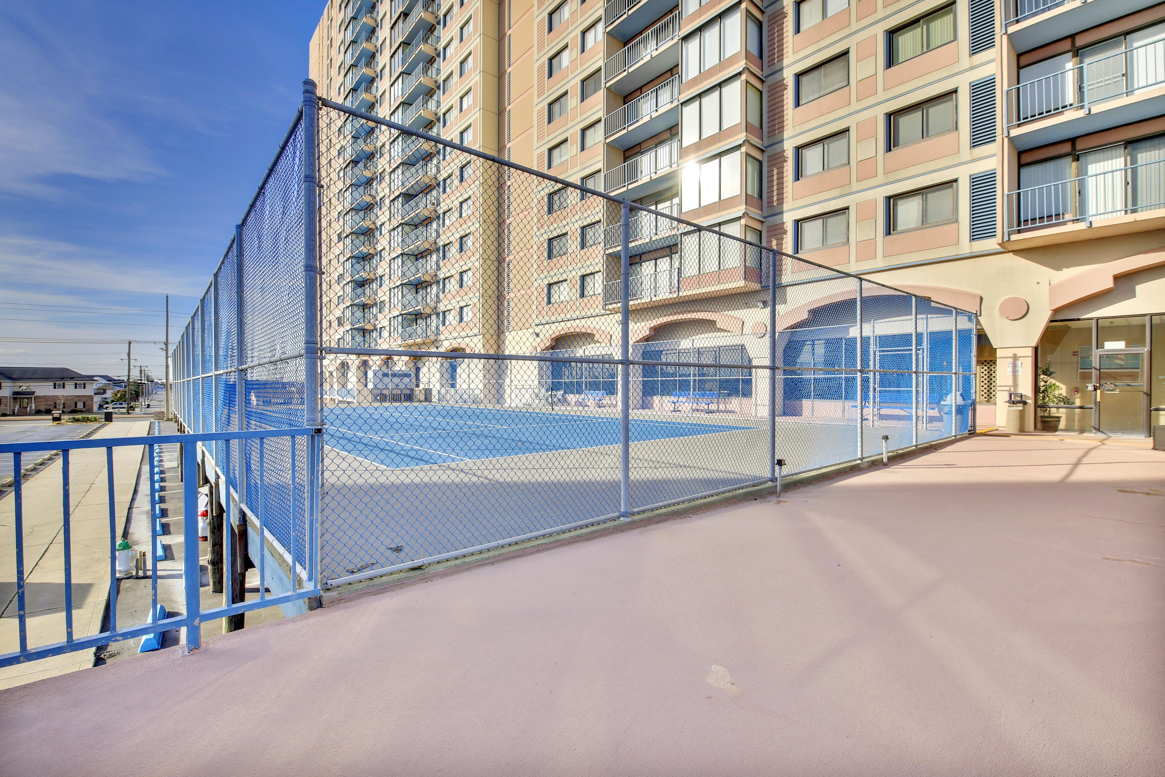 En bygning med flere etager, altaner, en indhegnet tennisbane og en parkeringsplads.
