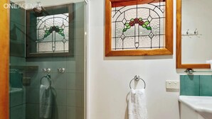 Un baño con cabina de ducha de vidrio, toallero blanco y una ventana con vitrales sobre el lavamanos.