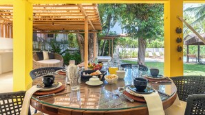 A dining area with a glass table, wicker chairs, and a view of a garden.