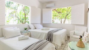 A hotel room with two beds, a chair, a small table, and a window with a view of greenery.