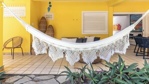 A yellow room with a hammock, wicker furniture, and a ceiling fan.