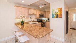 Cocina con encimeras de granito, una isla central con taburetes y armarios de madera, microondas y refrigerador.