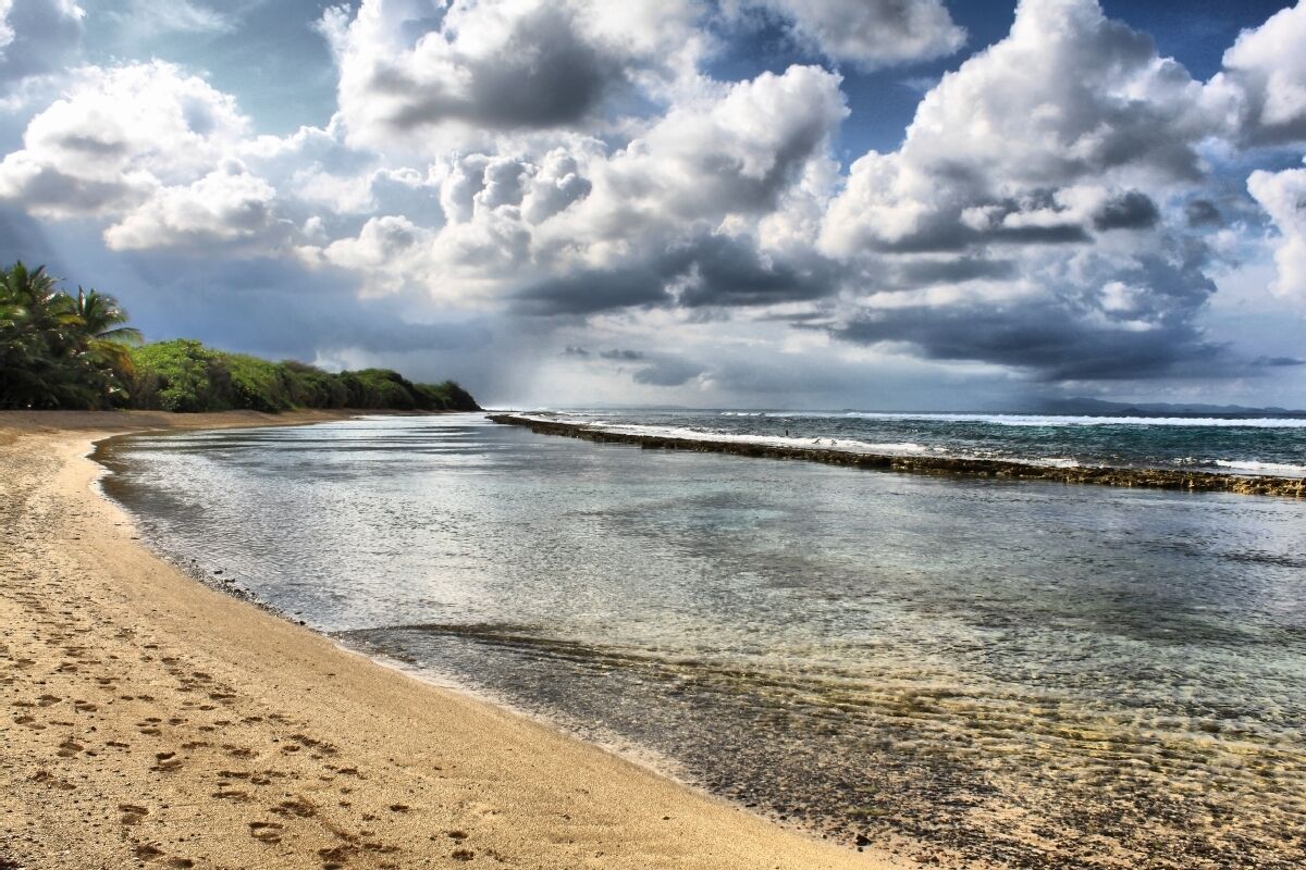 Una playa con agua cristalina, una orilla arenosa y cielo nublado.