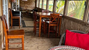 A wooden interior with a dining area, a round table with a mosaic top, and a view of palm trees through large windows. - Beautiful,Sandy Beach! 50 steps to the BEACH! Winter dates available book now! (Villa Borquien)