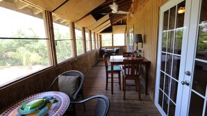 A covered outdoor area with wooden flooring, a dining table with chairs, and a large window offering a view of greenery. - Beautiful,Sandy Beach! 50 steps to the BEACH! Winter dates available book now! (Villa Borquien)