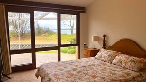Une chambre à coucher comprenant un lit, une table de chevet, une lampe et une vue sur l’extérieur grâce à de grandes fenêtres.