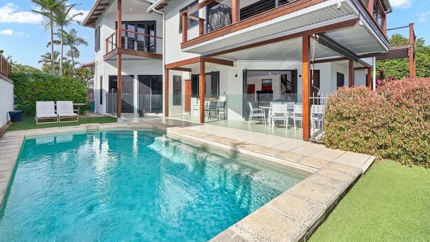 Ein modernes, zweistöckiges Haus mit Pool, Sitzgelegenheiten im Freien und einer überdachten Terrasse.
