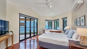 Ein Schlafzimmer mit einem großen Bett, einem Deckenventilator, einem Fernseher und Blick durch die Schiebetür.