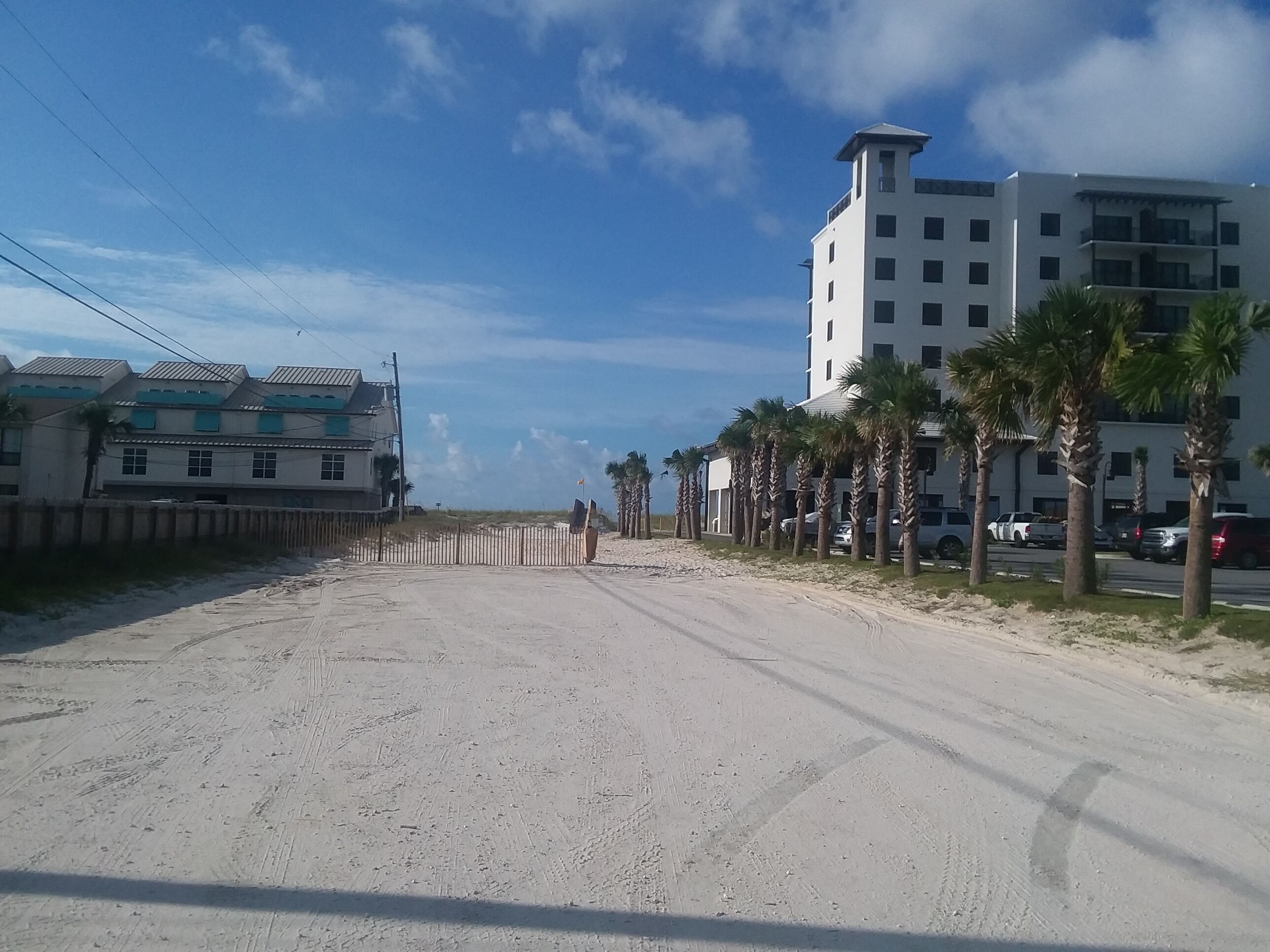 A sandy beach with buildings and palm trees.