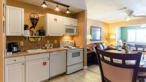 A compact kitchen with white cabinets, a microwave, a stove, and a sink. There is a dining area with a table and chairs, and a ceiling fan above. - Beach lover's paradise (Gulf Breeze)
