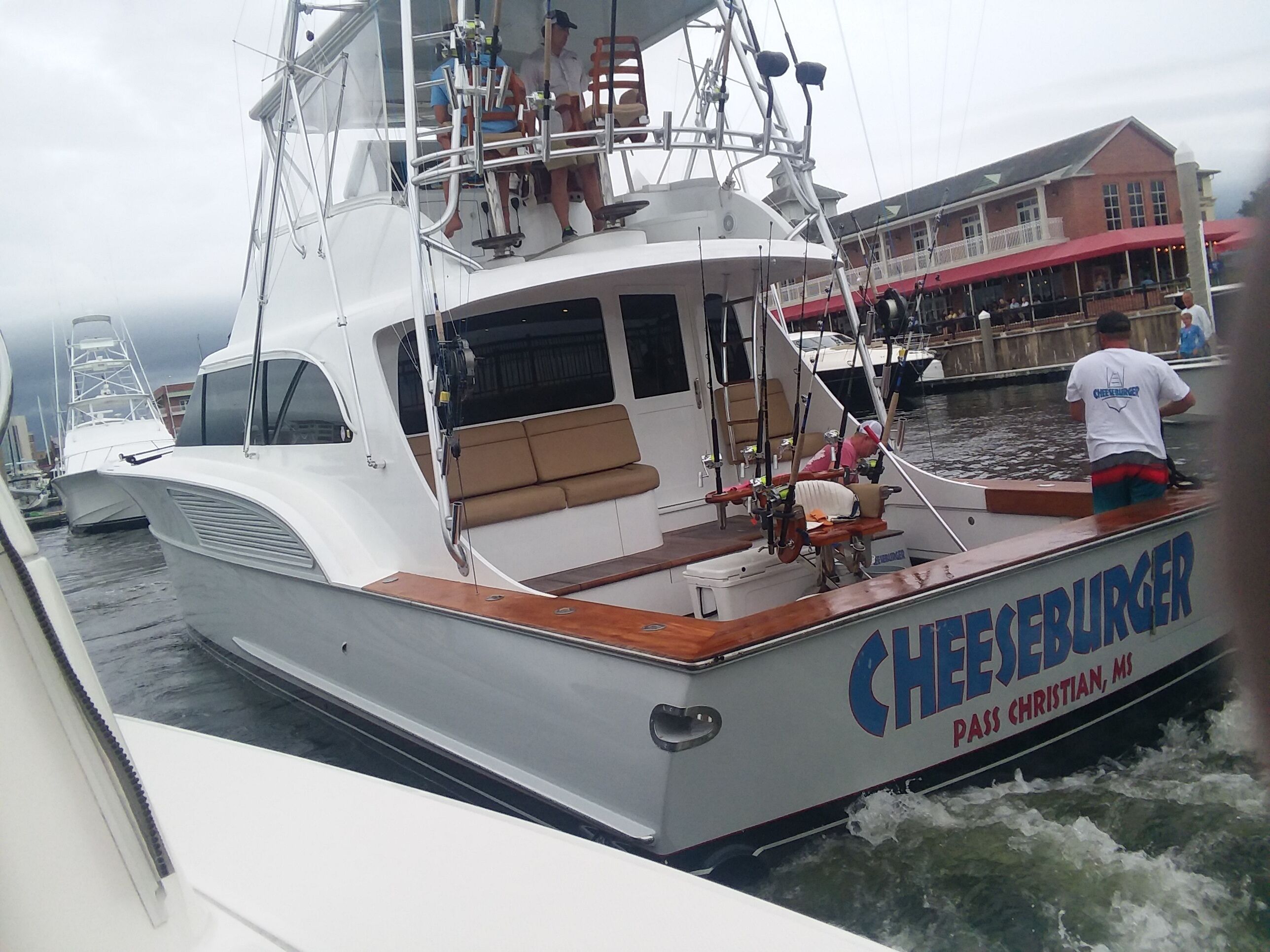 Een boot genaamd 'Cheeseburger' afgemeerd in een jachthaven met een overdekte zitplaats en een persoon die bij de achterkant staat.