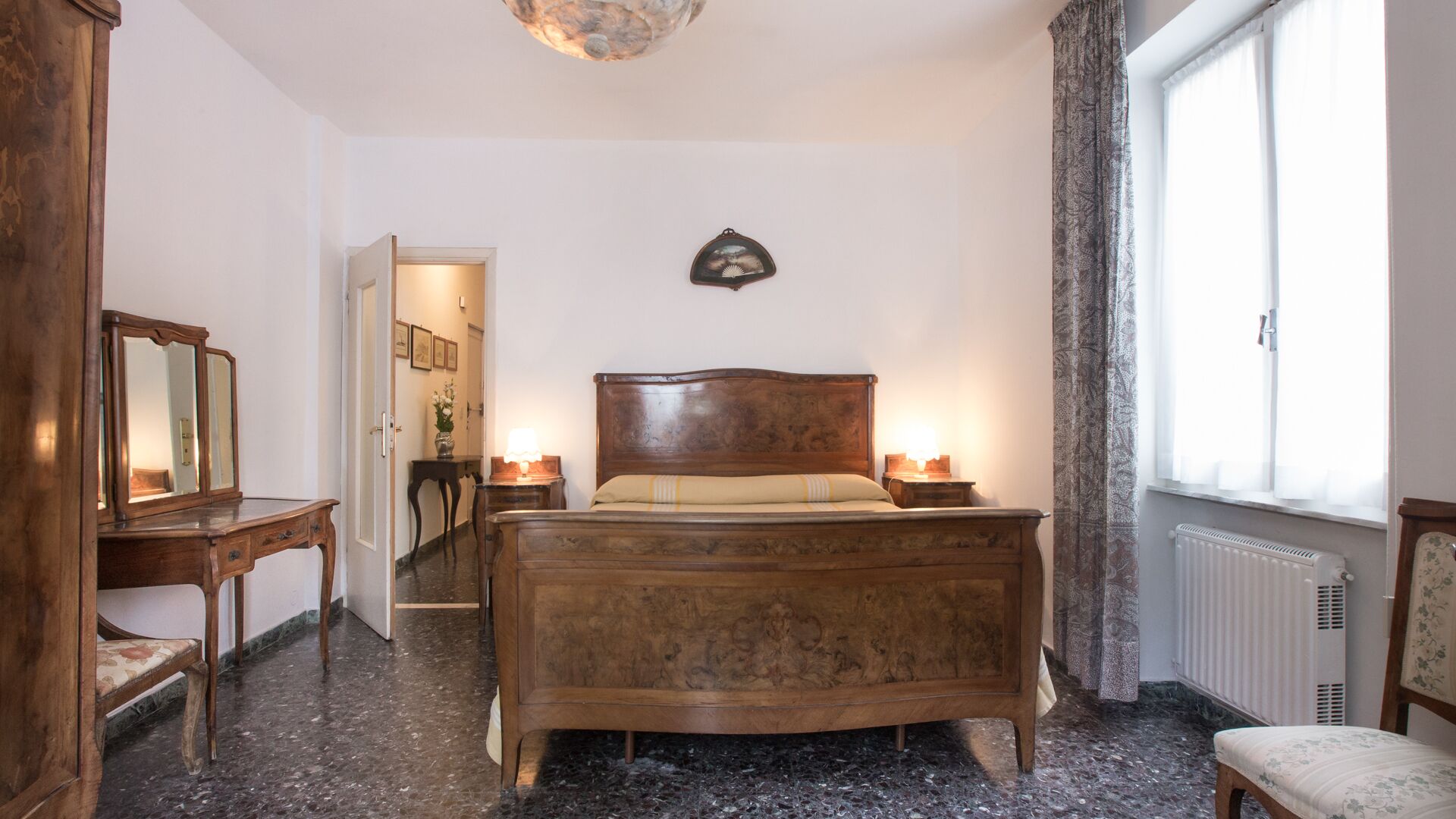 Een slaapkamer met een houten bed, nachtkastjes met lampen, een dressoir, een spiegel en een radiator.