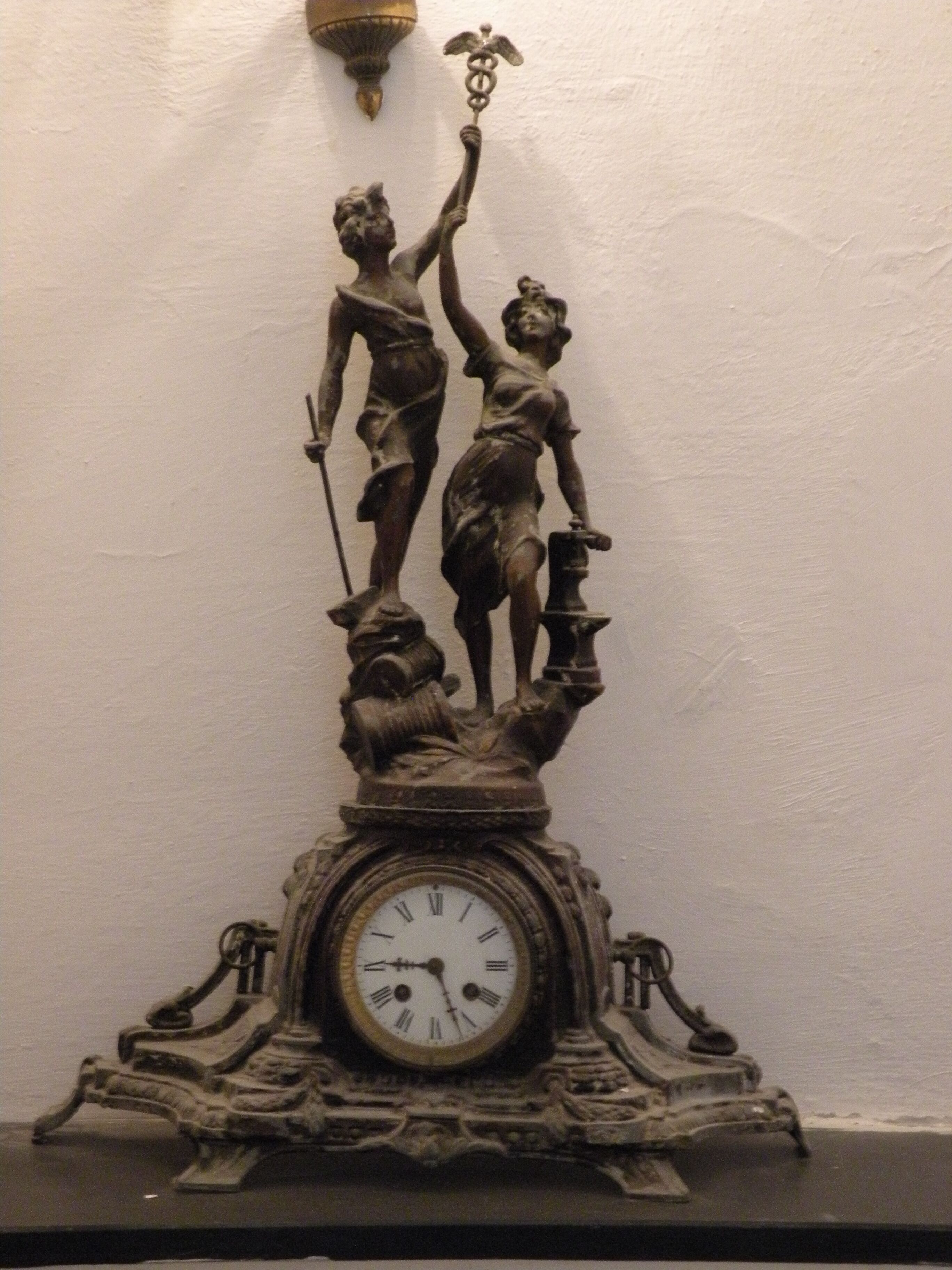 Een bronzen beeld van een man en een vrouw op een klokvoet, met een wandlamp erboven.