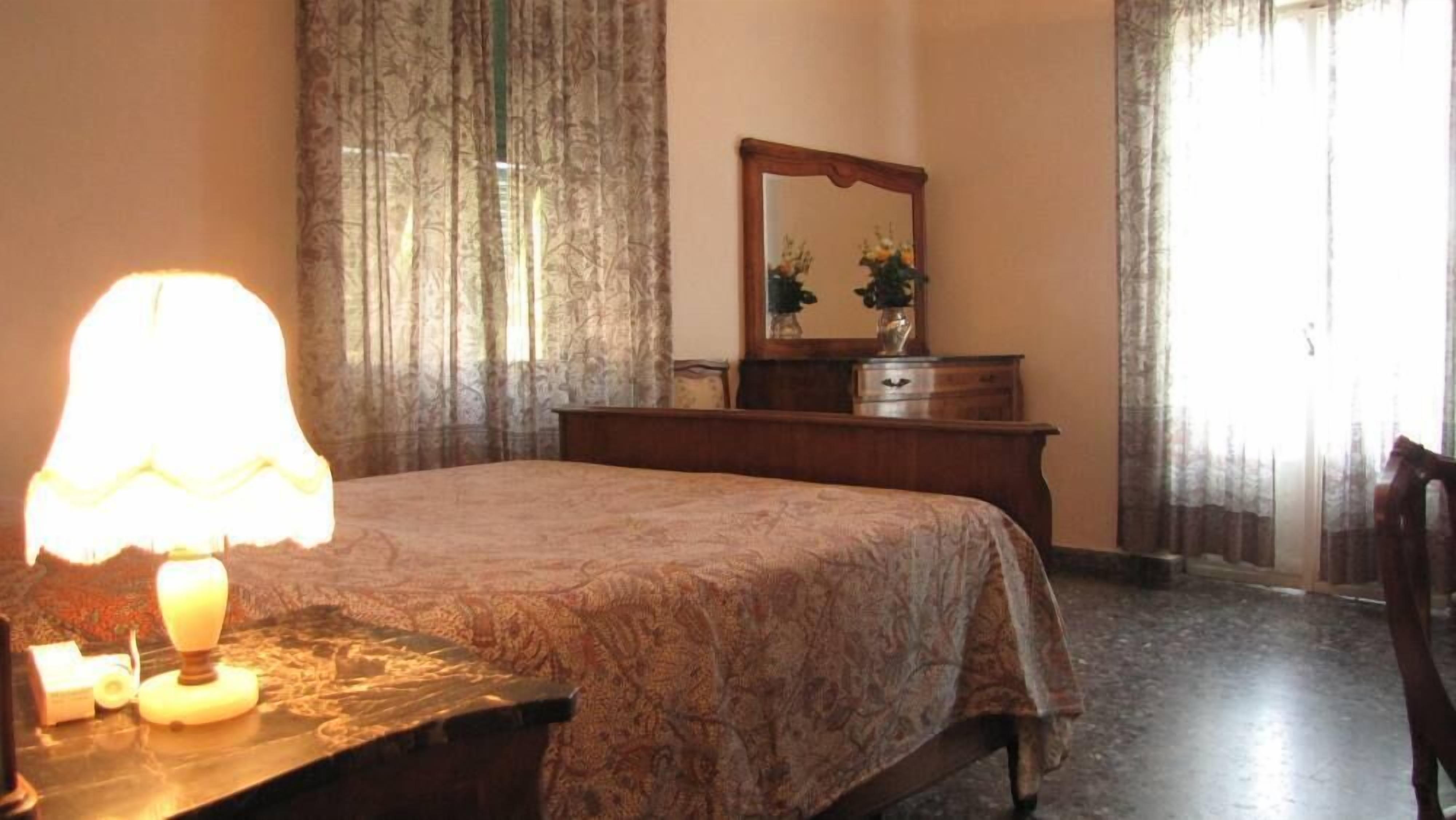 Ein Schlafzimmer mit einem Bett, einer Holzkommode, einem Spiegel und einer Lampe.
