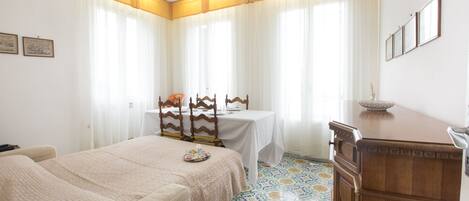 A hotel room with a bed, a table with chairs, a wooden cabinet, and a tiled floor.