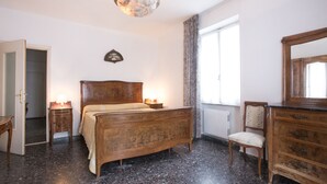 A bedroom with a wooden bed, bedside lamps, a radiator, a chair, and a dresser. - Charming historical 4 guests apartment stunning sea view free wi- fi parking  (Monterosso al Mare)
