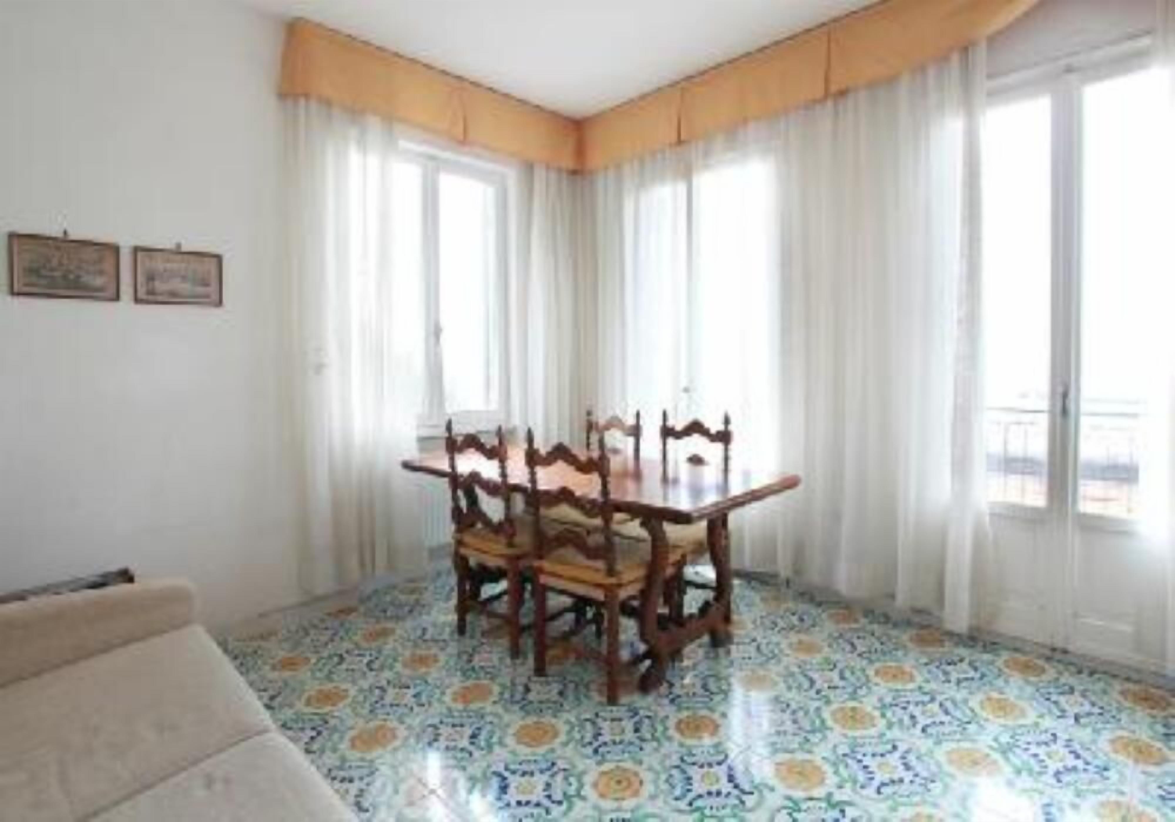 A dining area with a table and chairs, a patterned floor, and large windows with curtains.