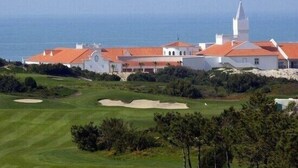 Ein Golfplatz mit Clubhaus und Turm, umgeben von viel Grün und Blick aufs Meer.