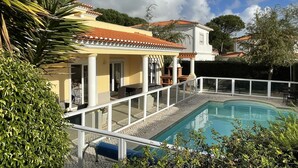 Ein Poolbereich mit überdachter Terrasse und umgebender Bepflanzung.