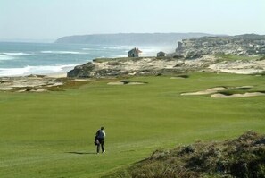 Een kustgolfbaan met uitzicht op de oceaan en rotsachtige kliffen op de achtergrond.