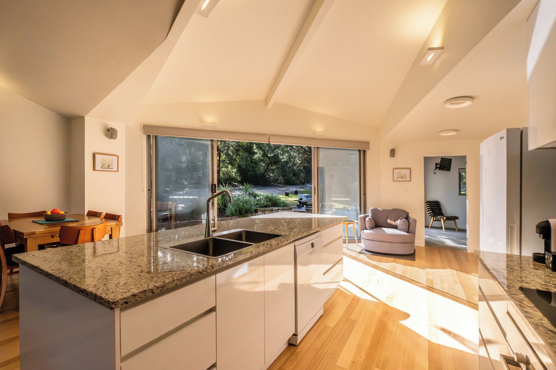 A modern kitchen with a large island, a dining area with a table and chairs, and a view of the outdoors through a sliding door.