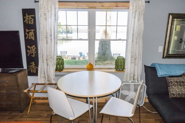 A room with a round table, two chairs, a sofa, a TV, and a window with curtains.