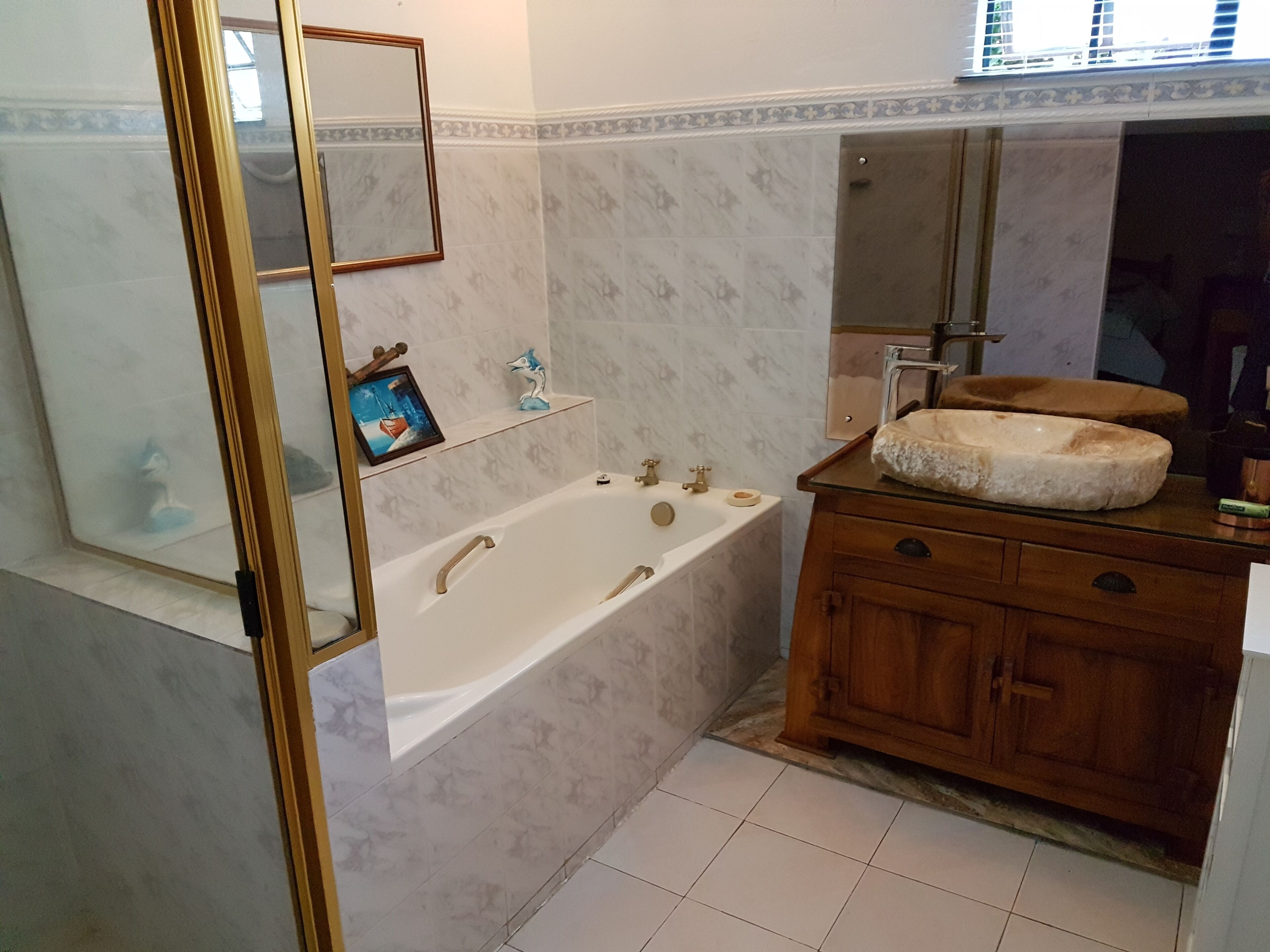Une salle de bain avec une baignoire, un meuble-lavabo en bois, des carreaux de marbre, un tableau encadré et une décoration sur le thème des bateaux.