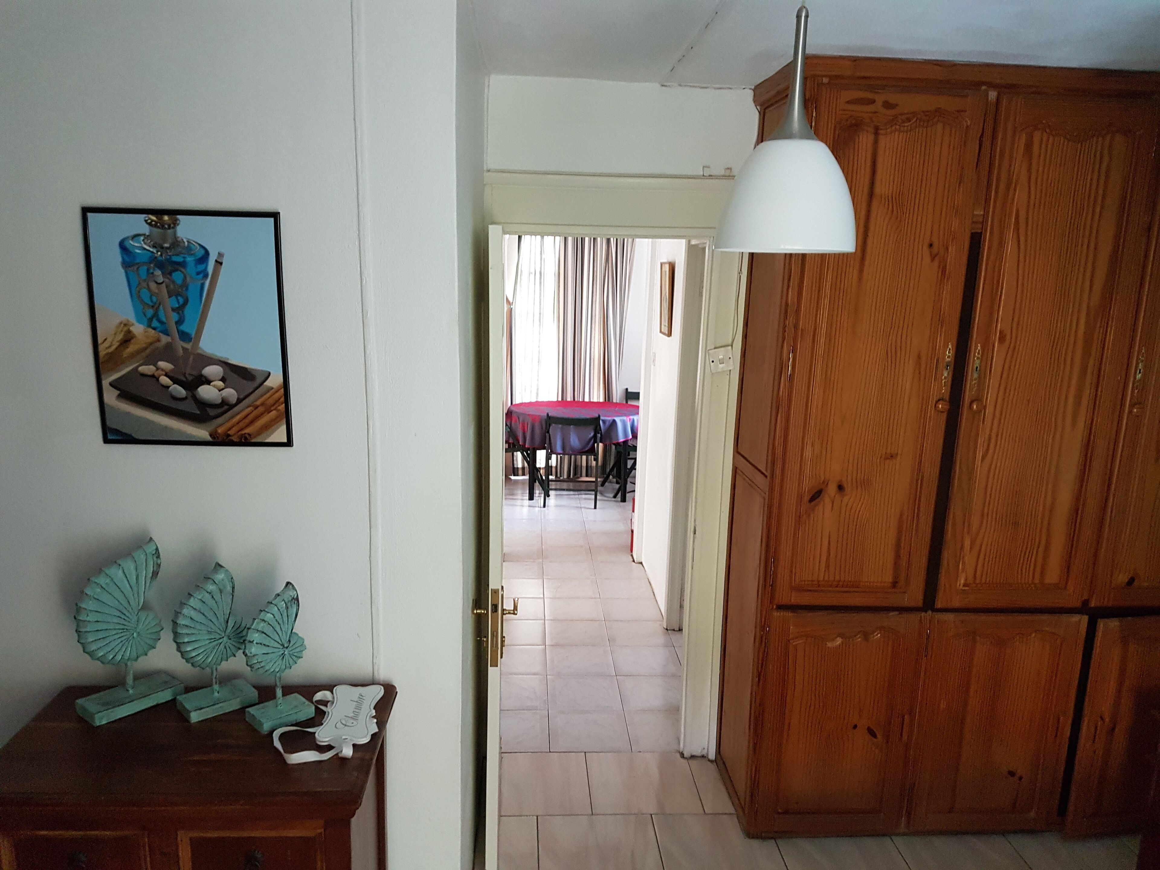 A room with a wooden wardrobe, a table with a red tablecloth, and a framed picture on the wall.
